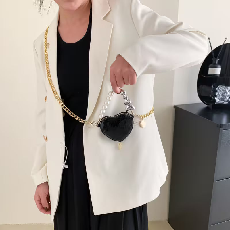 Person holding a black heart-shaped handbag with gold chain strap in an indoor setting.