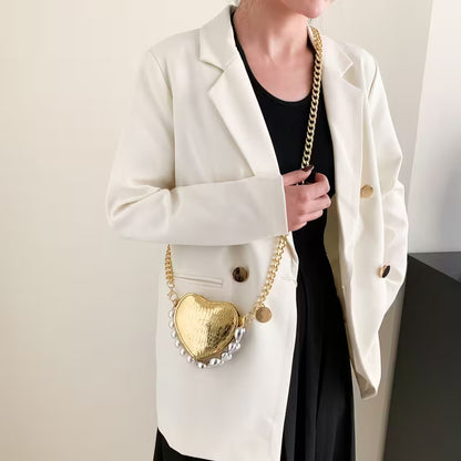 Person wearing a white blazer holding a gold heart-shaped handbag.