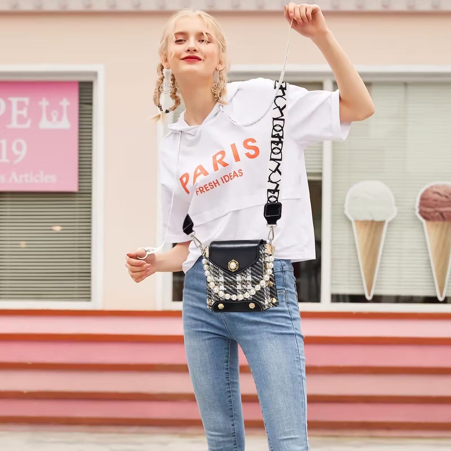 Woman holding a black handbag with decorative elements in front of an ice cream shop.