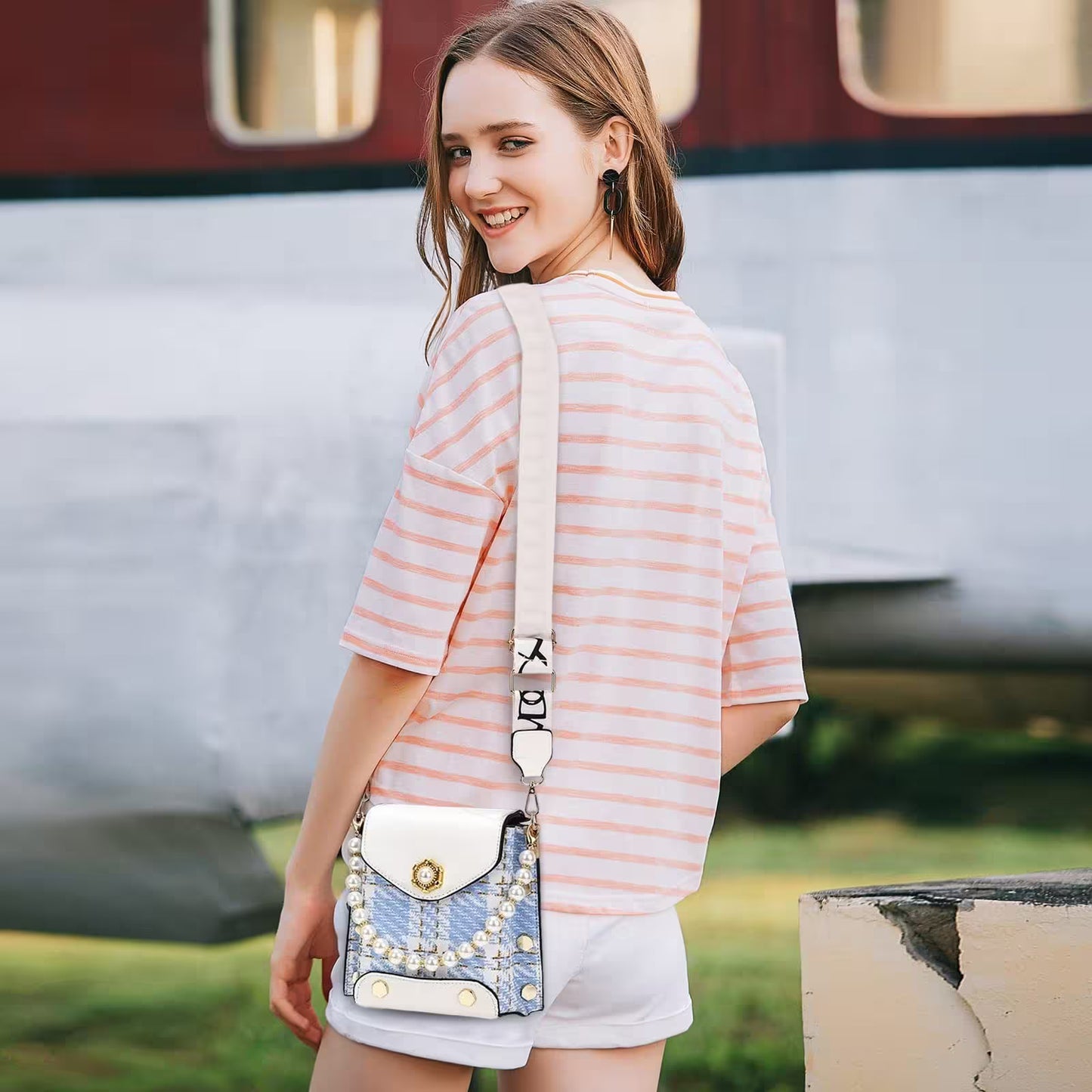 Woman in a striped shirt with a decorative handbag standing in front of a vintage vehicle.
