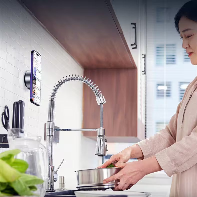 Woman washing dishes in a modern kitchen with a smartphone displaying an app.