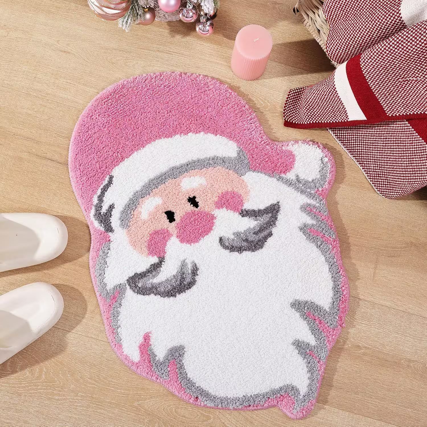 Pink Santa Claus bath mat on a wooden floor with Christmas decor.