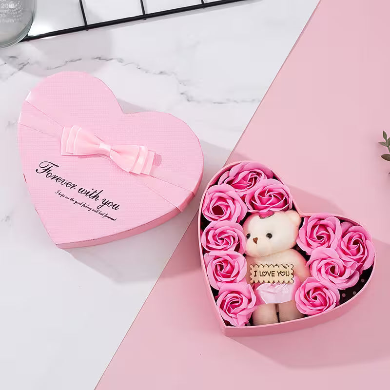 Heart-shaped pink box with a teddy bear and pink roses on a marble surface