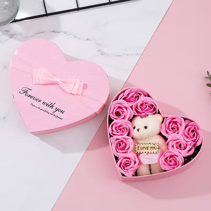 Heart-shaped pink box with a teddy bear and pink roses on a marble surface