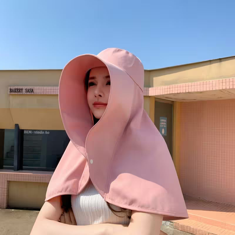 Person wearing a pink hooded garment in front of a building with a clear blue sky.