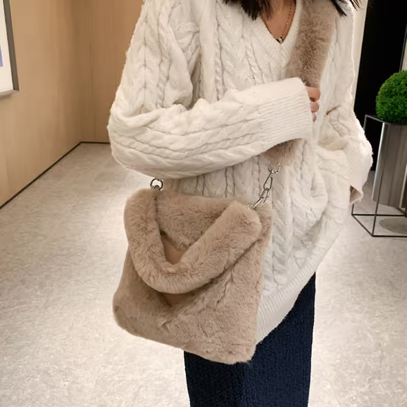 Person wearing a white cable knit sweater holding a beige handbag indoors.