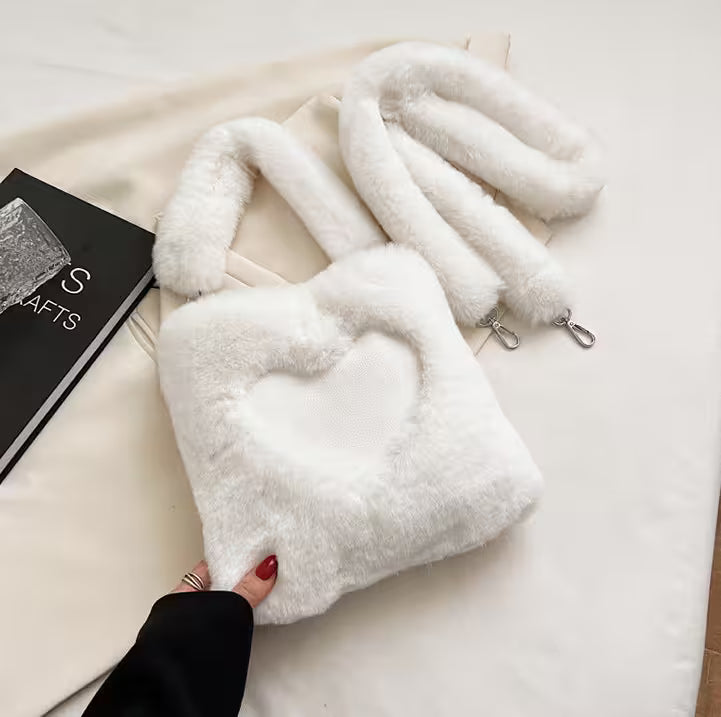 White fluffy handbag on a light surface with a book and a hand visible.