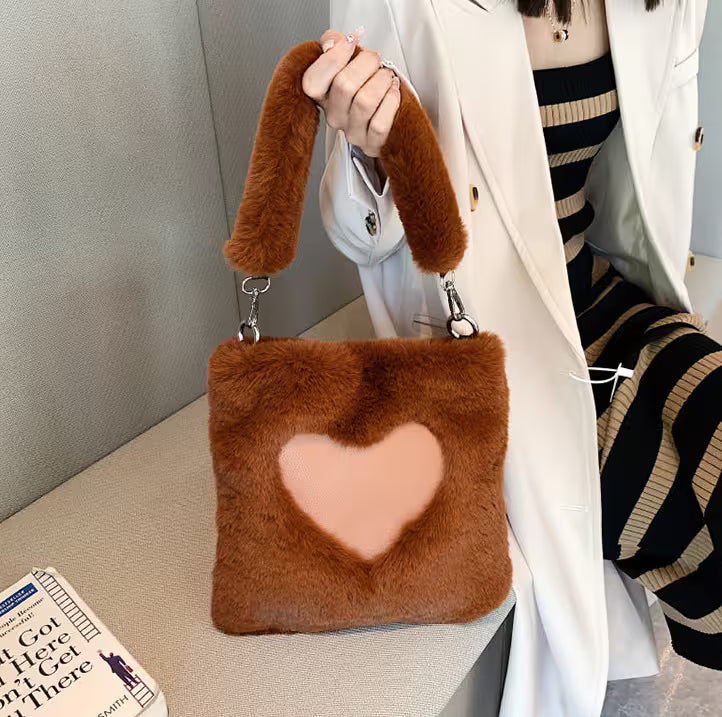 Brown fur bag with a heart design held by a person, with a book on a surface in the background.