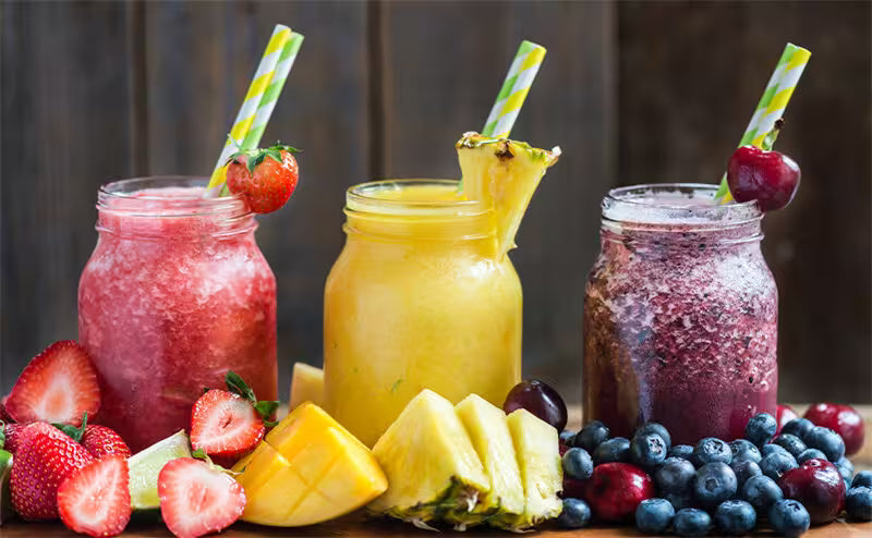 Three colorful smoothies in jars with fruit and straws on a wooden surface