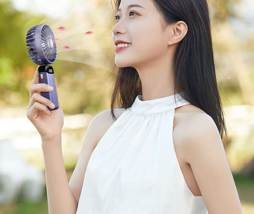 Woman holding a handheld fan outdoors with a blurred natural background