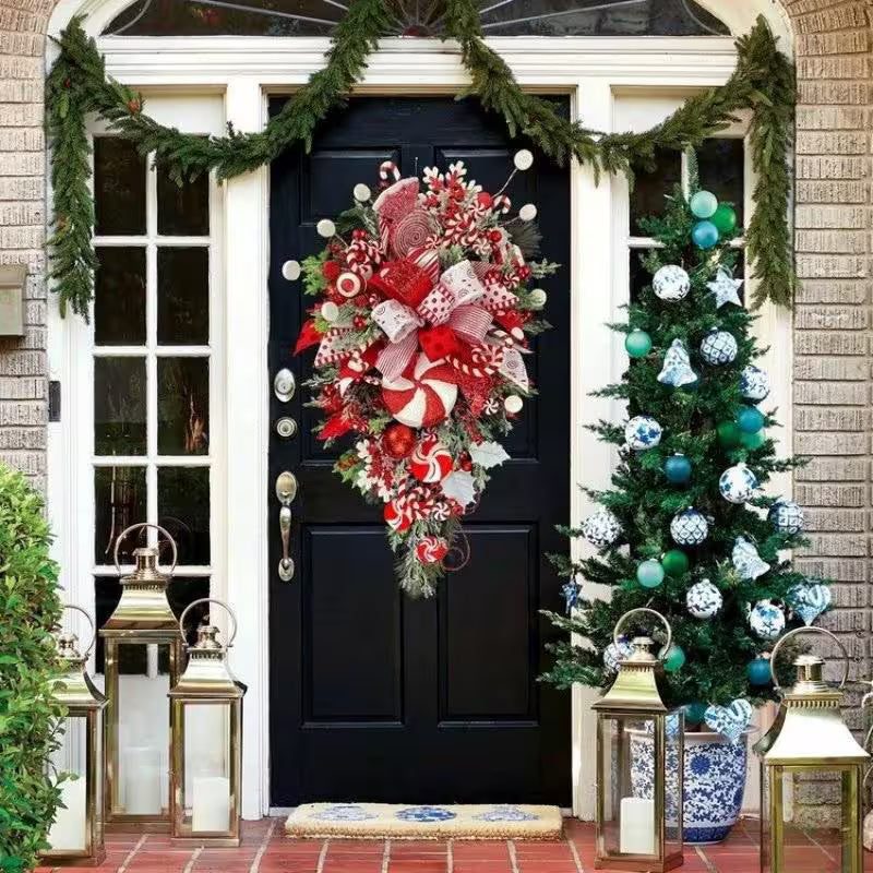 Decorative Christmas wreath and tree on a black door with lanterns and garlands.