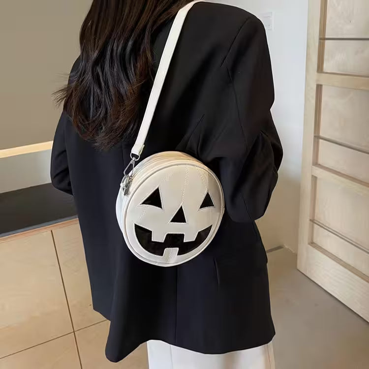 Person wearing a black outfit with a white round bag featuring a jack-o'-lantern face design.