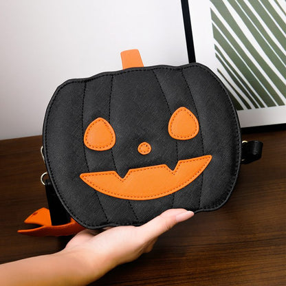 Black pumpkin-shaped bag with orange face held by a hand on a wooden surface.