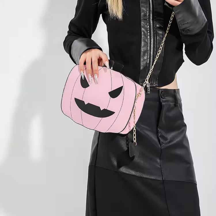 Person holding a pink pumpkin-shaped bag with black details on a plain background