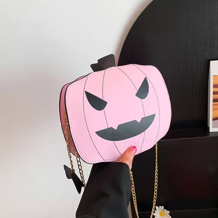 Pink pumpkin-shaped bag with a face design held by a hand against a neutral background