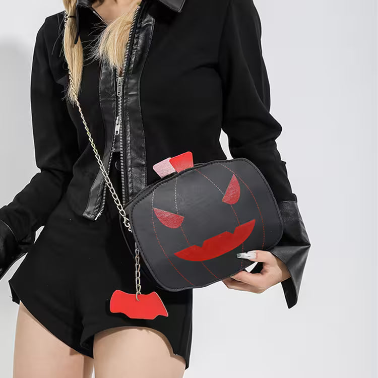 Person holding a black bag with red accents resembling a jack-o'-lantern face on a plain background