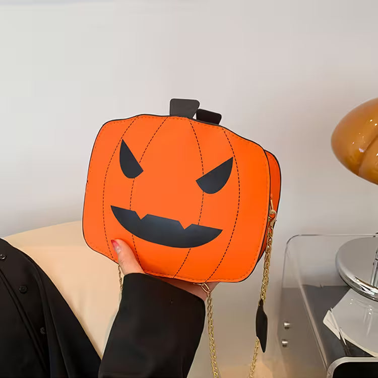 Pumpkin-shaped handbag with a face design held by a person indoors.