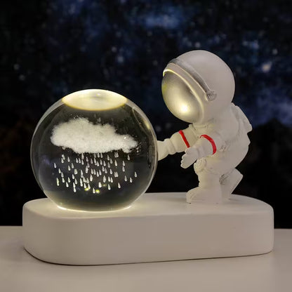 Astronaut figurine interacting with a crystal ball containing a cloud and raindrops on a dark background.