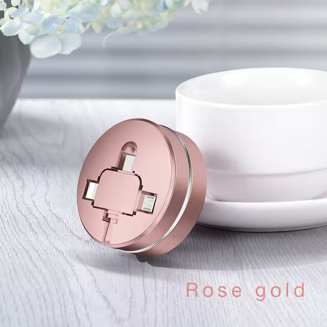 Rose gold compact mirror on a light surface with a white container and blurred flowers in the background.