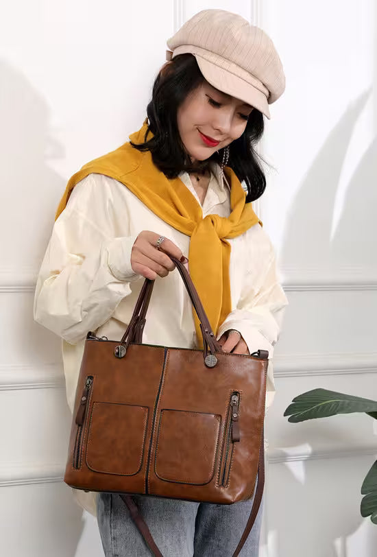 Woman holding a brown leather handbag wearing a beige cap and yellow scarf against a white wall.
