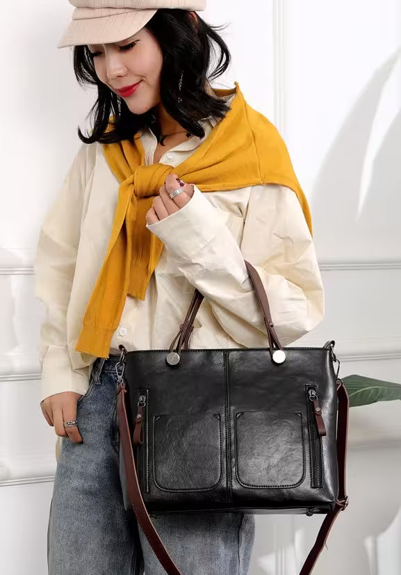 Woman holding a black leather handbag with a yellow scarf and beige hat indoors.