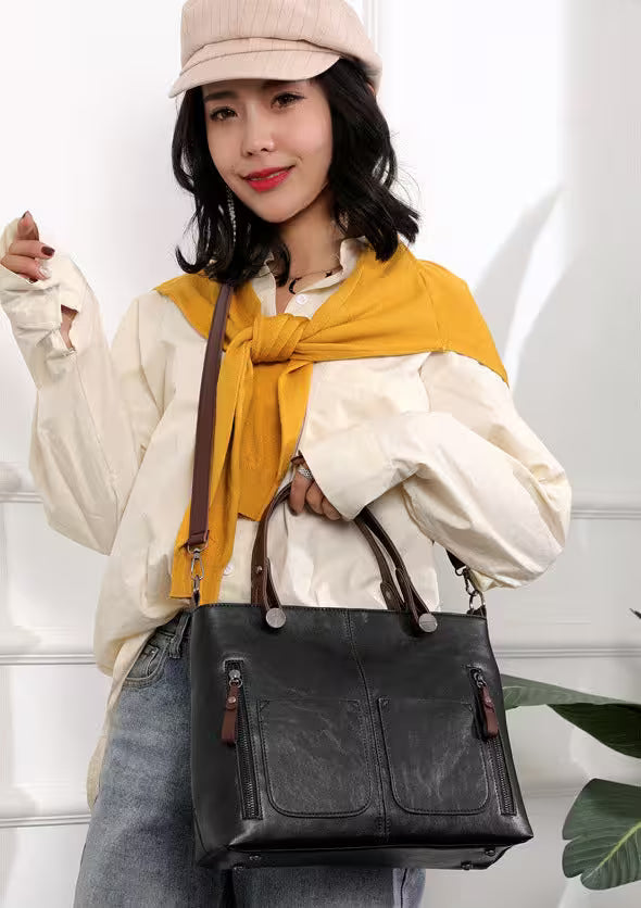 Woman wearing a beige cap, yellow scarf, and holding a black leather handbag against a white background.