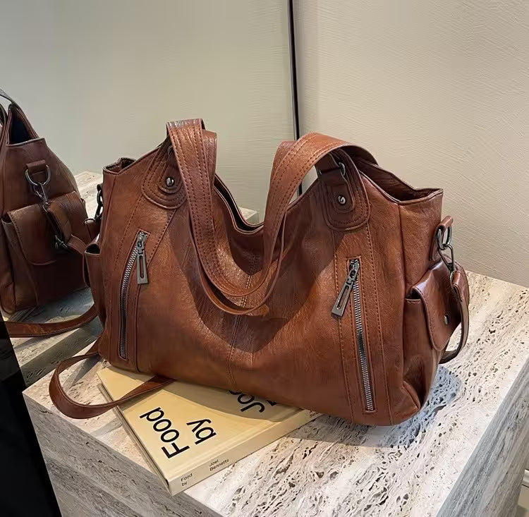 Brown leather handbag on a stone surface with a book underneath