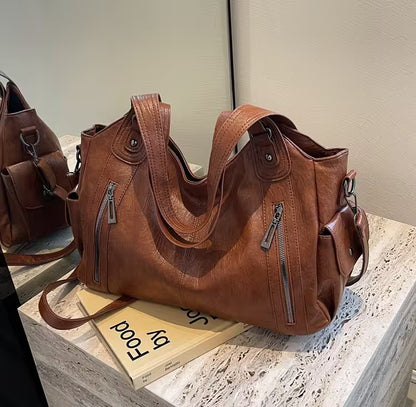 Brown leather handbag on a stone surface with a book underneath