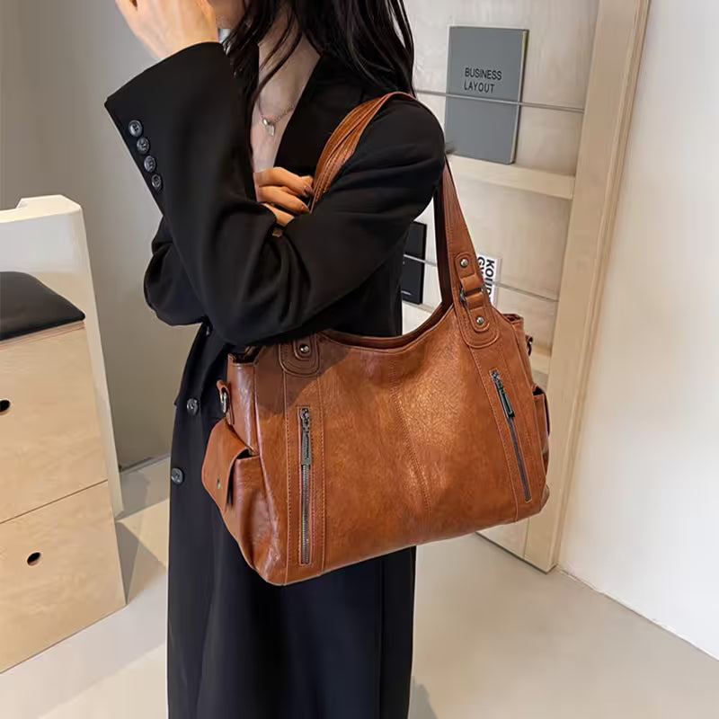 Person holding a brown leather handbag in an indoor setting