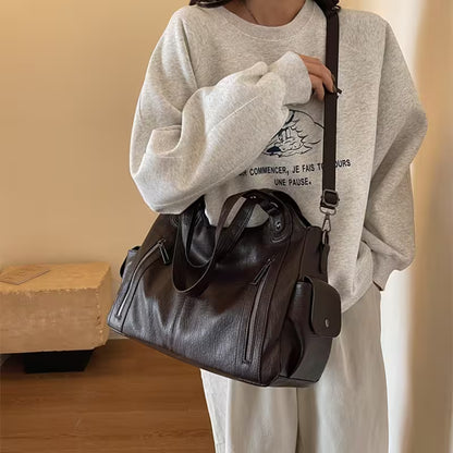 Person wearing a gray sweatshirt with a graphic design, holding a brown leather bag indoors.