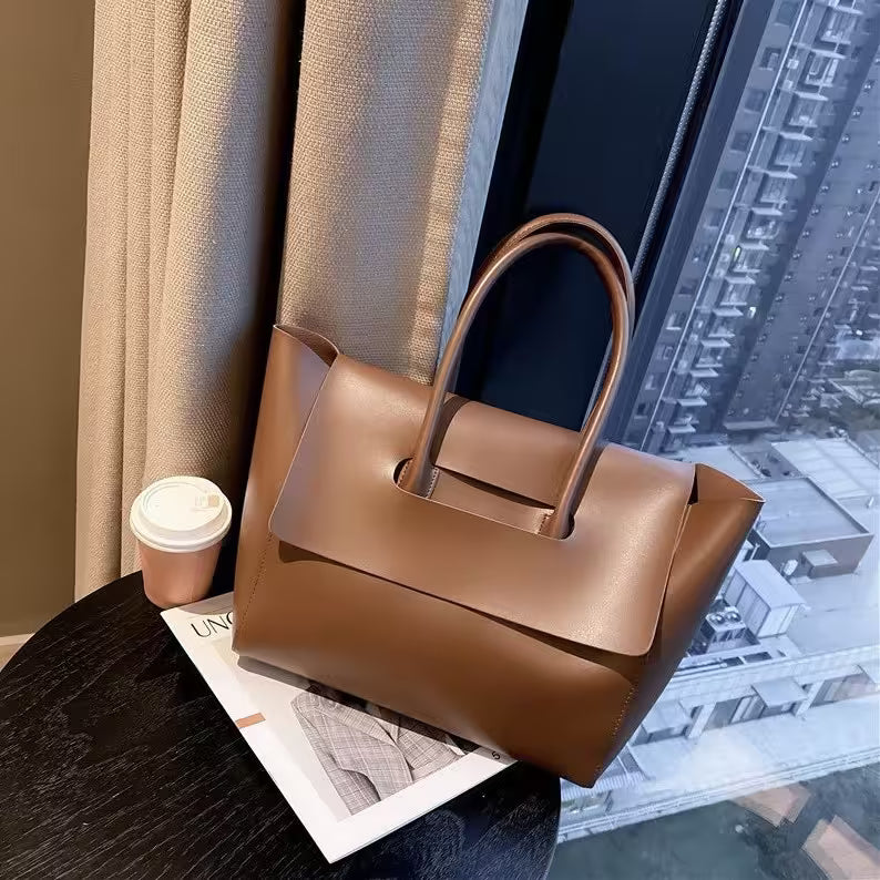 Brown handbag on a table with a cityscape view through a window.