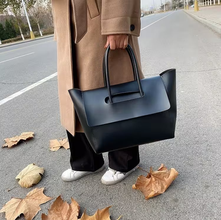 Person holding a black handbag on a road with fallen leaves