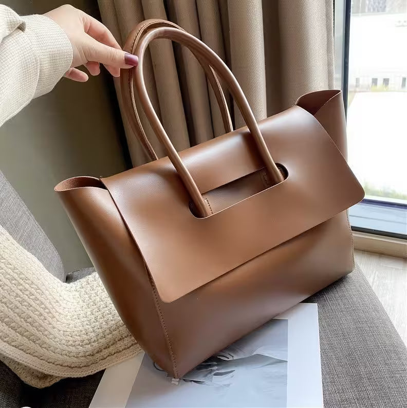 Brown leather handbag held by a person indoors with curtains in the background