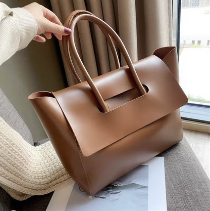 Brown leather handbag held by a person indoors with curtains in the background