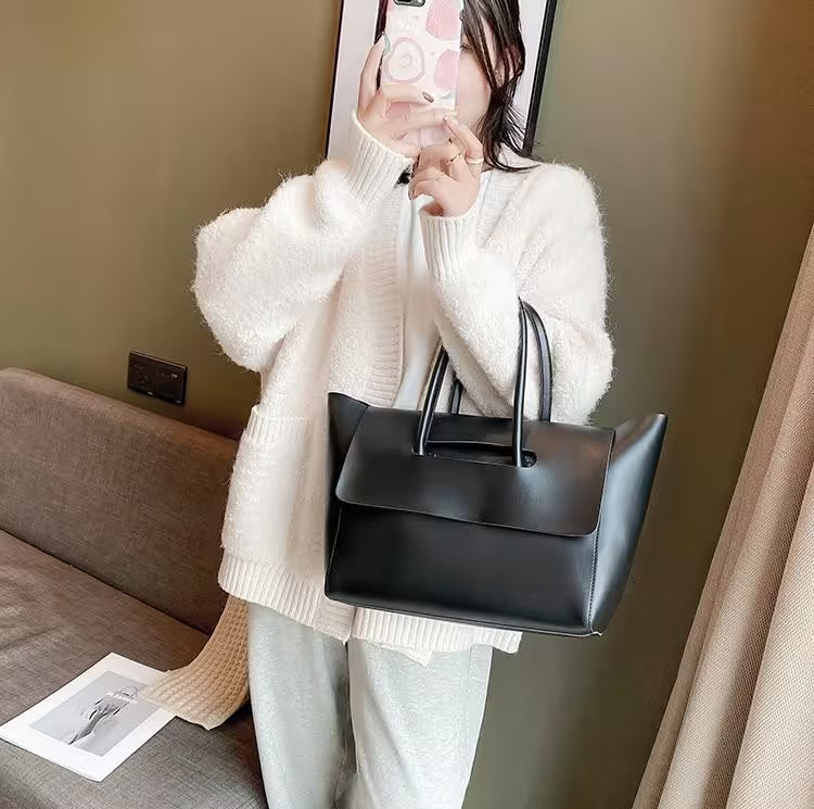 Person holding a black handbag in a room with a couch and wall socket.