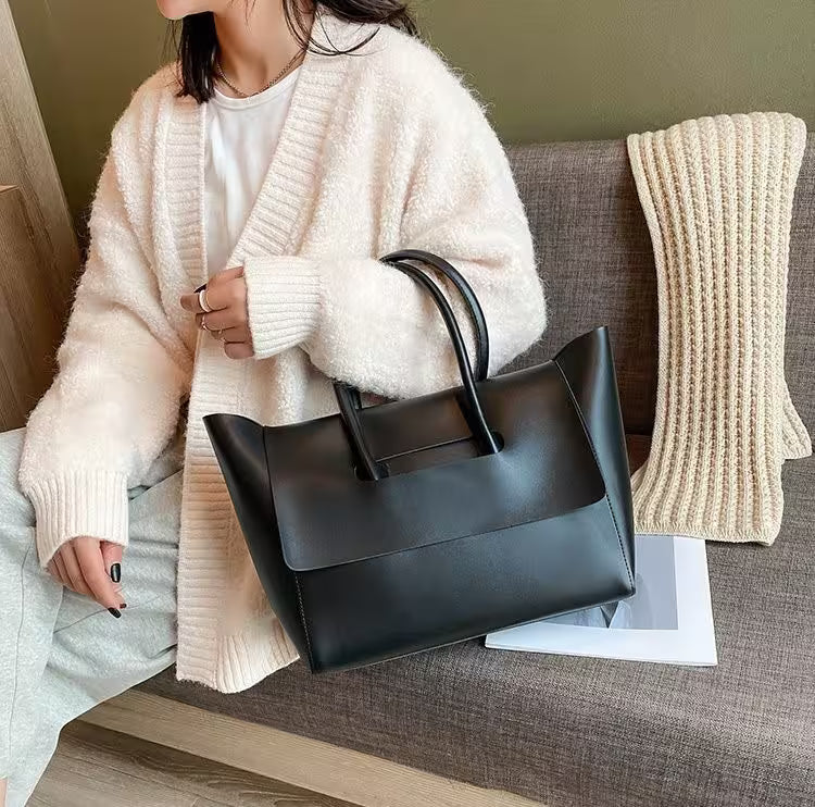 Person holding a black handbag on a couch with a beige blanket