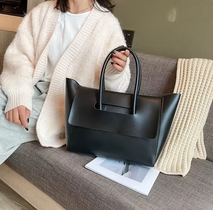 Person holding a black handbag on a gray couch with a white blanket