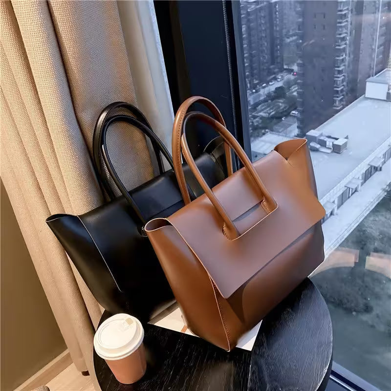 Two handbags, one black and one brown, on a surface with a cityscape view through a window.