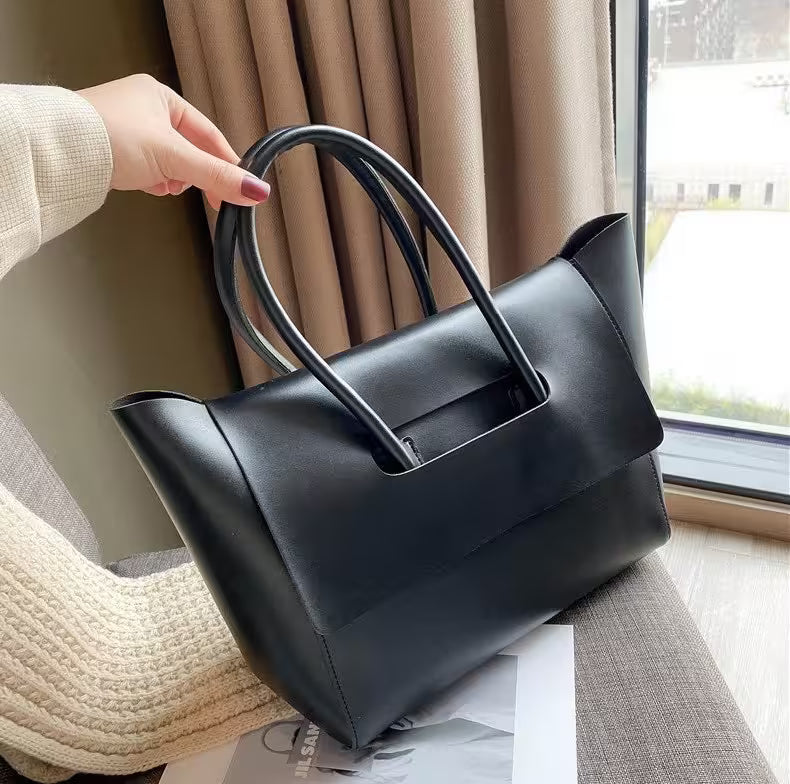 Black handbag held by a hand in front of a window with curtains.