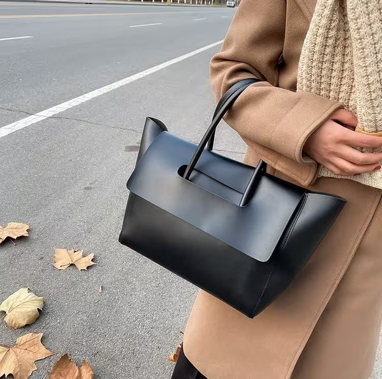 Person holding a black handbag on a street with leaves on the ground