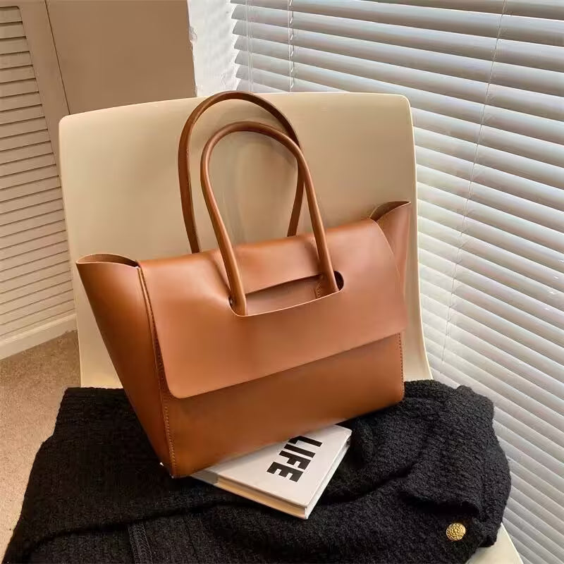 Brown leather handbag on a chair with a magazine underneath