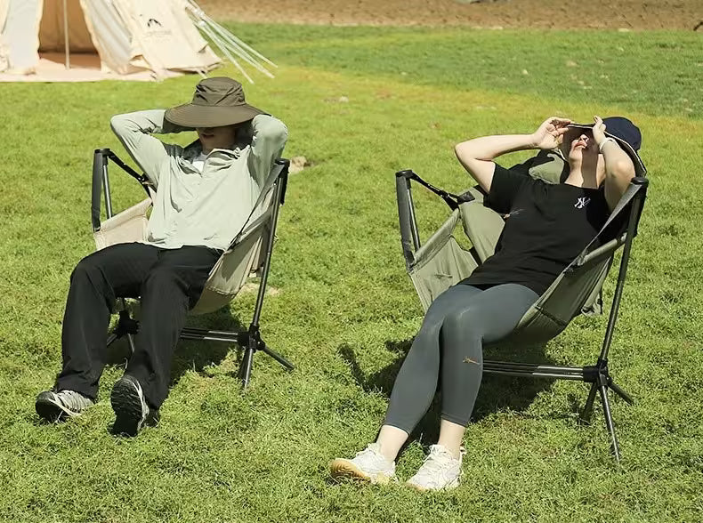 Two people relaxing on camping chairs in a grassy field.