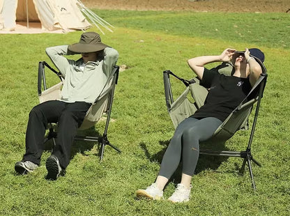Two people relaxing on camping chairs in a grassy field.