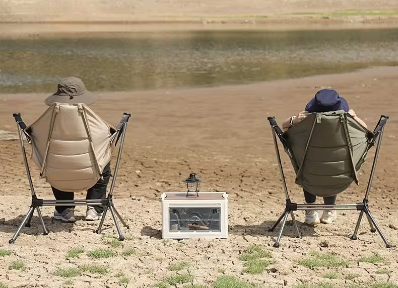 Two people sitting in folding chairs by a body of water, with a small table between them.