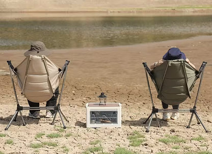 Two people sitting in folding chairs by a body of water, with a small table between them.