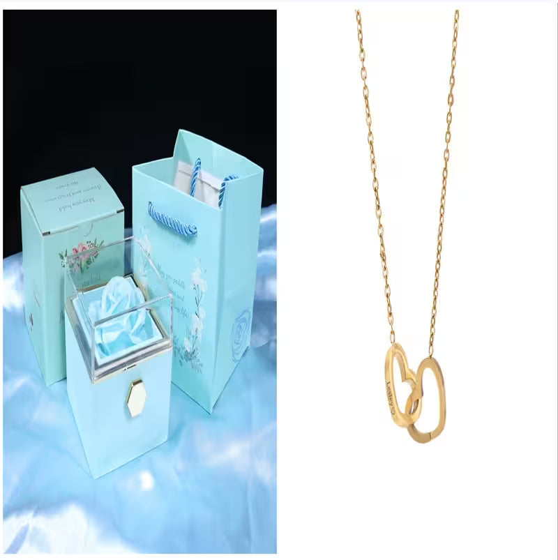 Gold necklace with interlocking heart pendants next to a blue jewelry box with floral design.
