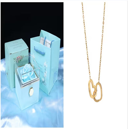 Gold necklace with interlocking heart pendants next to a blue jewelry box with floral design.