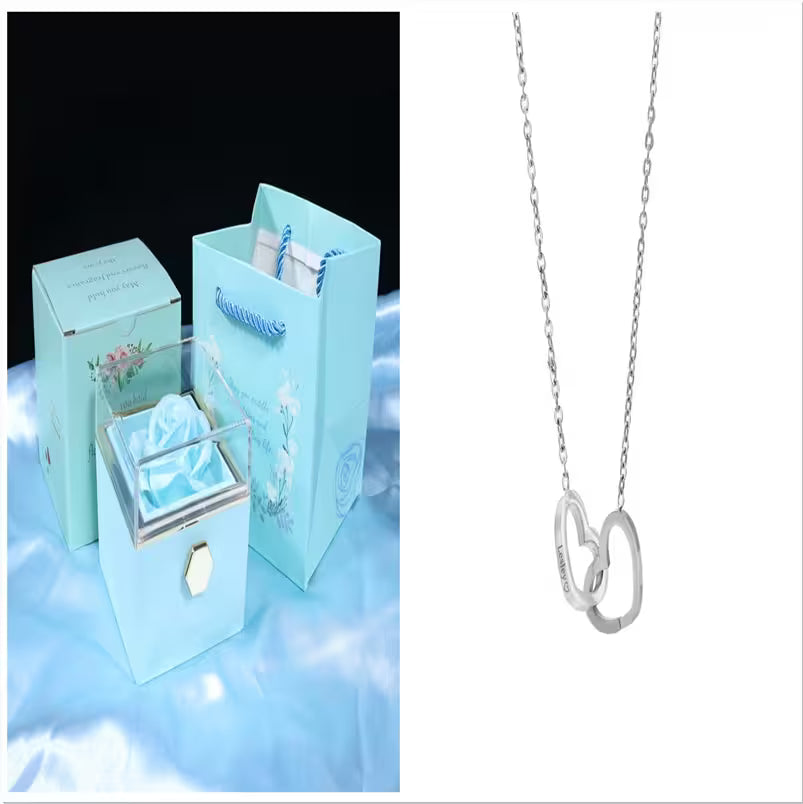 Silver necklace with interlocking heart pendants on a white background, next to a turquoise jewelry box and bag.