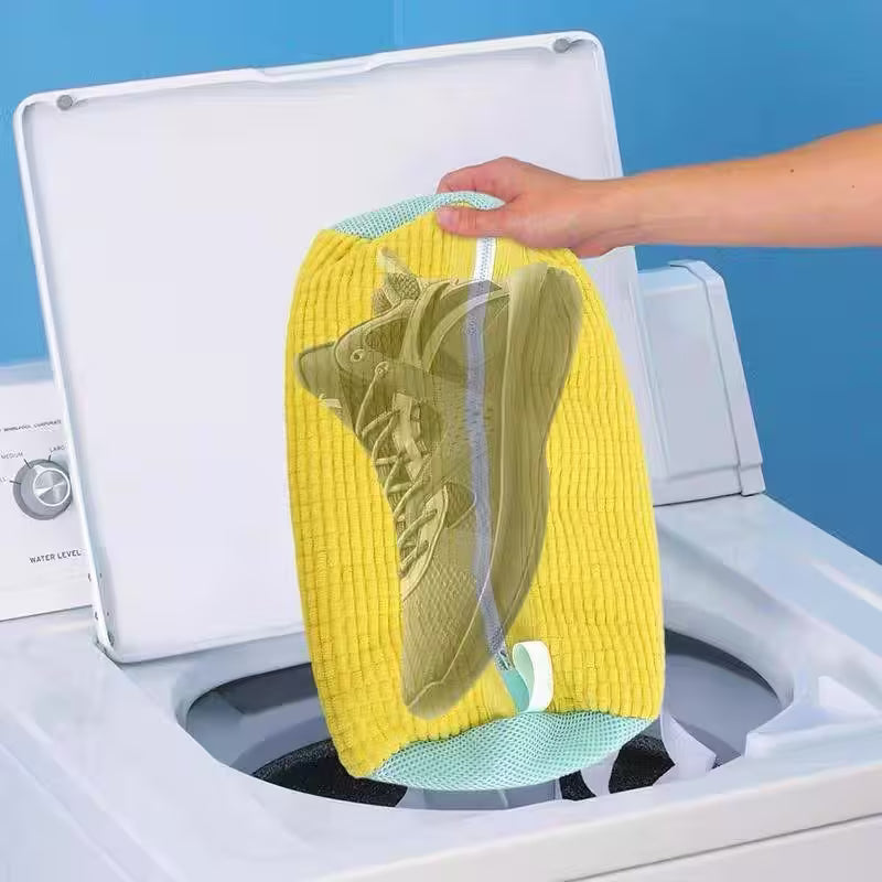Person placing a yellow towel with green shoes inside a washing machine.