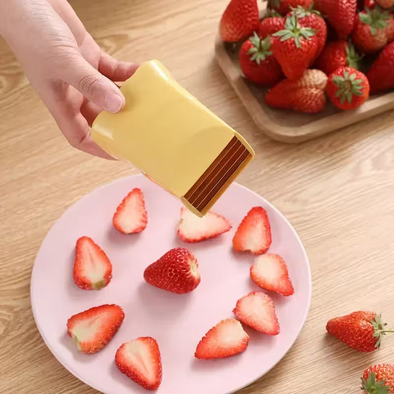 Hand using a yellow strawberry picker on a plate with sliced strawberries, surrounded by whole strawberries.
